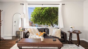 A living room with a leather sofa, a coffee table, a lamp, and a view of a tree through a window. - Vintage Charm 3BR Home w,Yard, Pets Welcome (Shoreline)