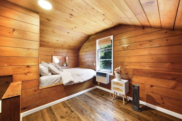 A cozy bedroom with a wooden ceiling, a bed, a bedside table, a nightstand, and a window.