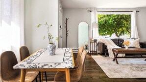 A dining area with a table set for four, a vase with flowers, and a view of a tree outside. - Vintage Charm 3BR Home w,Yard, Pets Welcome (Shoreline)