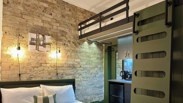 Ein Schlafzimmer mit Backsteinwand, einem Etagenbett, einem Schreibtisch mit Stuhl und einer grünen Tür.