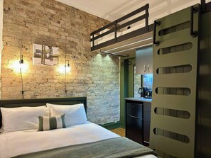 Une chambre avec un mur en briques, un lit superposé, un bureau avec une chaise et une porte verte.