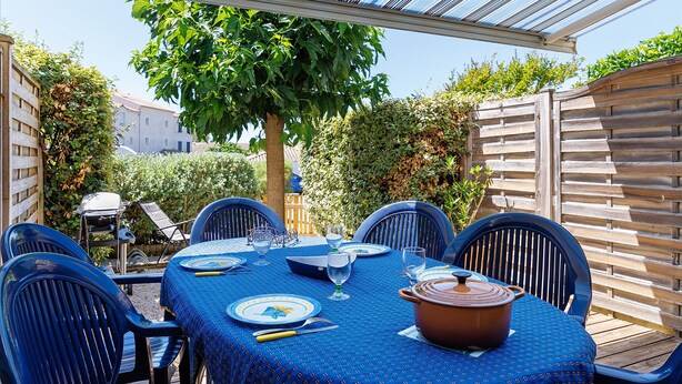 En udendørs patio med et spisebord, omgivet af stole, under en pergola.