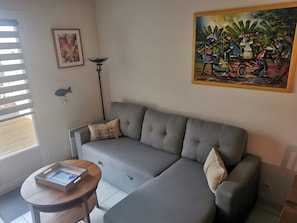 Un canapé gris, une petite table ronde avec un plateau, une lampe sur pied, un tableau encadré et une grande peinture.