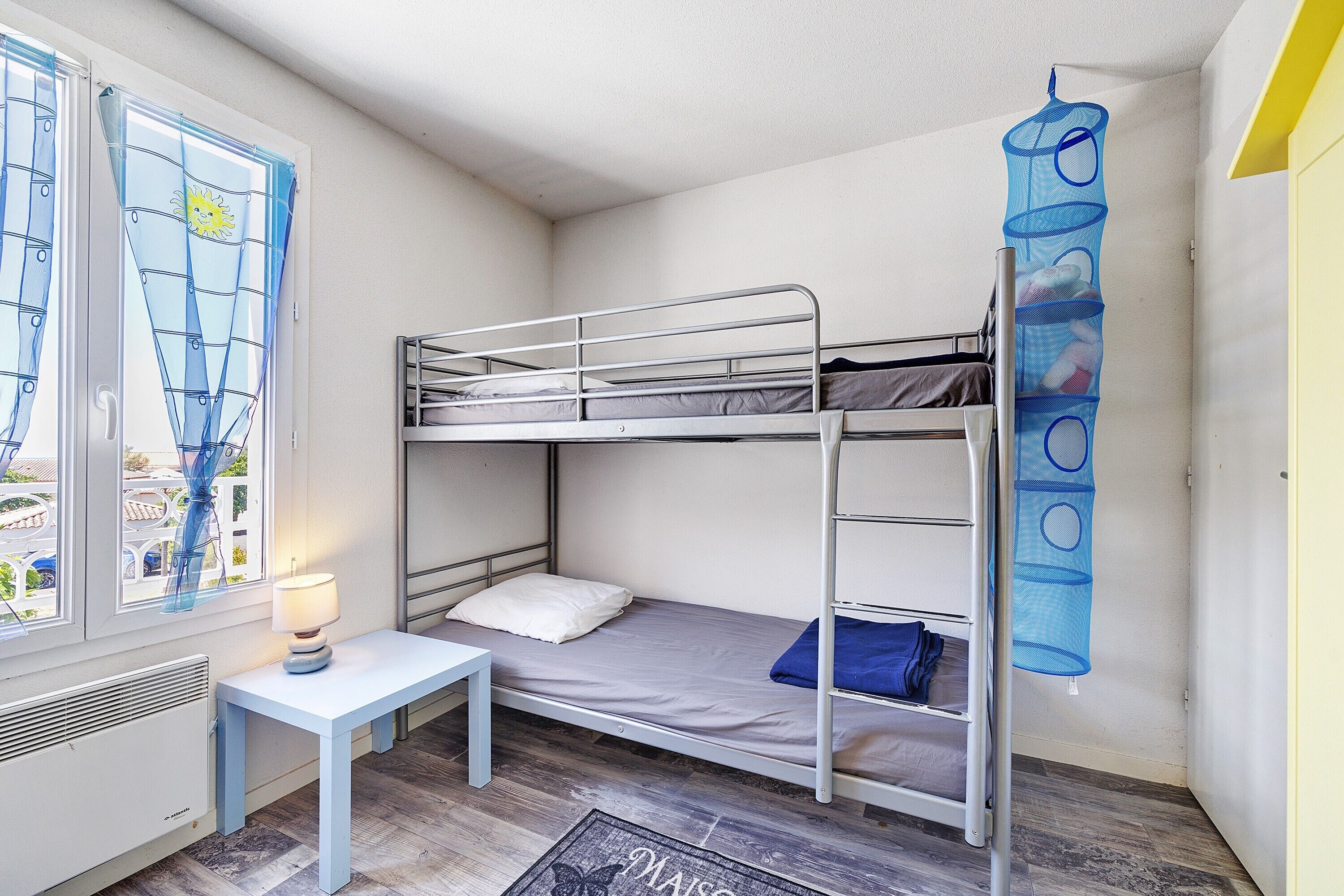 A bunk bed room with a window, a table, and a hanging storage unit.