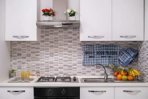 A modern kitchen with white cabinets, a tiled backsplash, a gas stove, a sink, and a fruit bowl.
