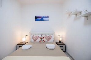 Ein Schlafzimmer mit einem Bett, zwei Nachttischen mit Lampen, einem Wandbild und herzförmigen Kissen.