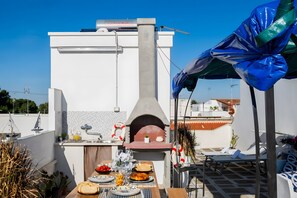 Eine Außenküche mit Pizzaofen, Esstisch gedeckt mit Speisen und Sonnenschirm.