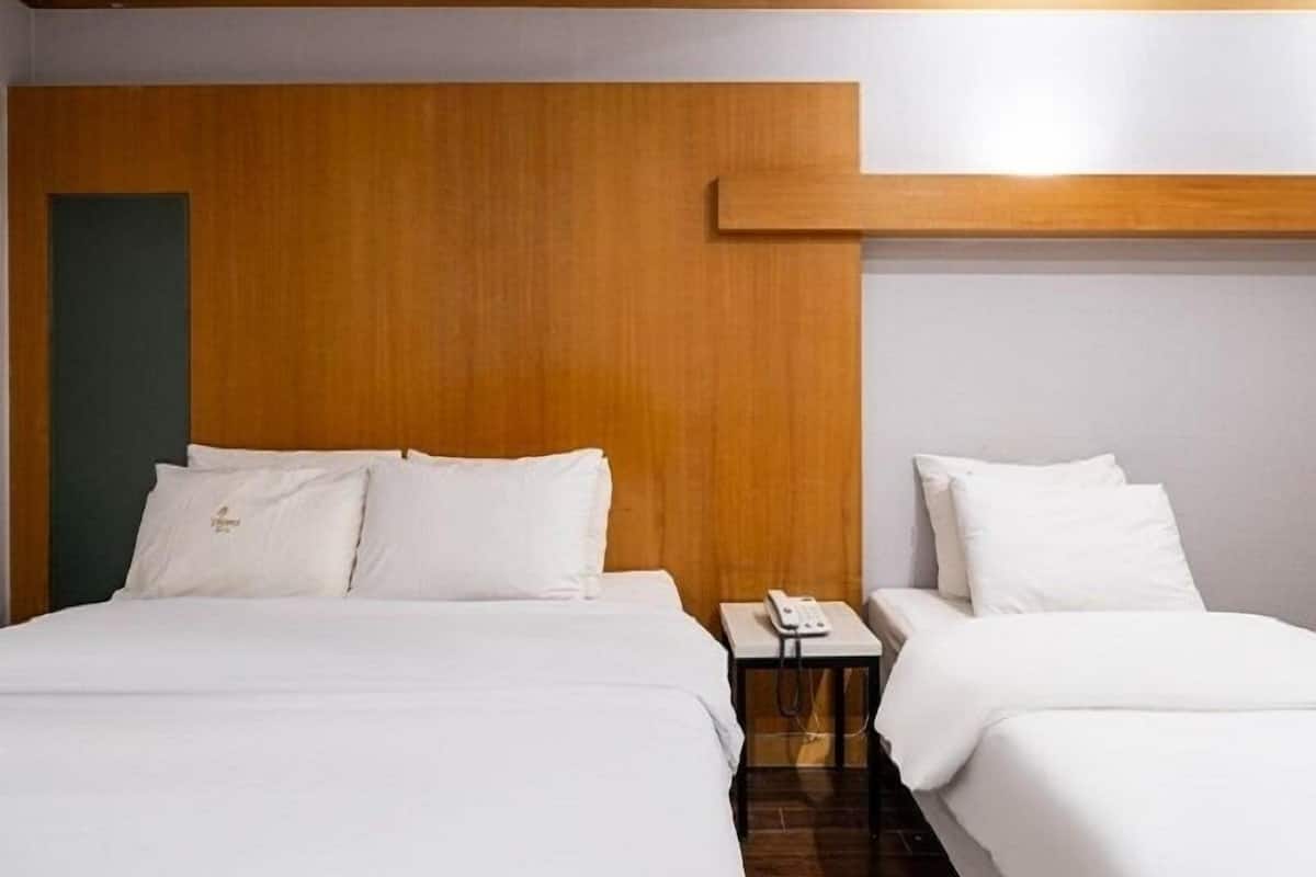 A hotel room with two beds, a wooden headboard, a bedside table with a phone, and a small nightstand.