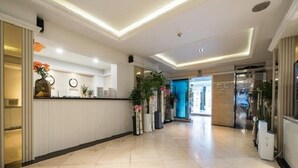 Eine geräumige Lobby mit einer Rezeption, einer Uhr und Zimmerpflanzen.