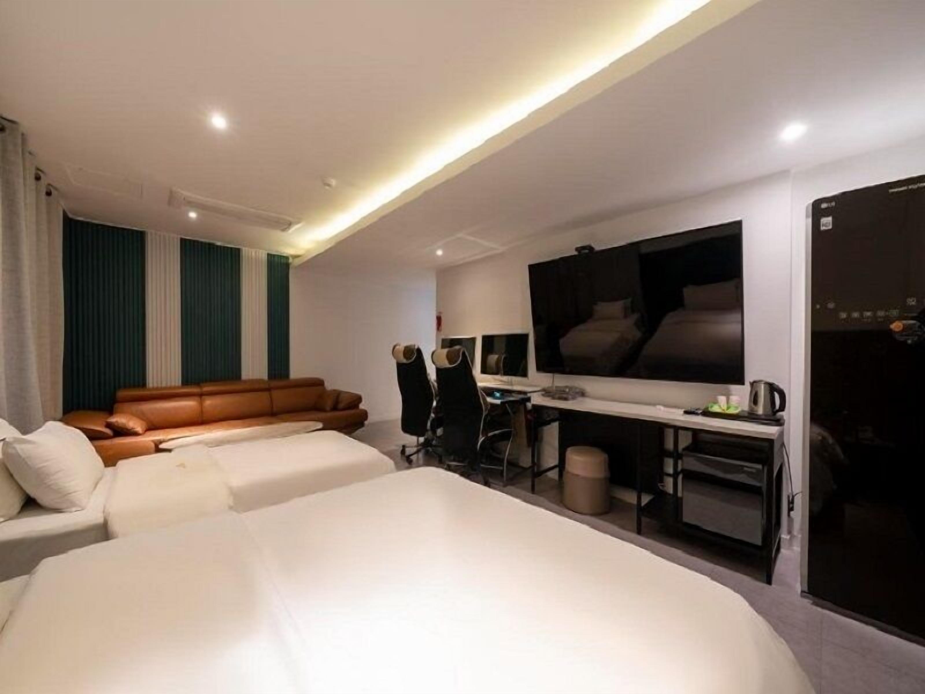 Una habitación de hotel moderna con una cama grande, un sofá, un escritorio con silla, un televisor y un minibar.