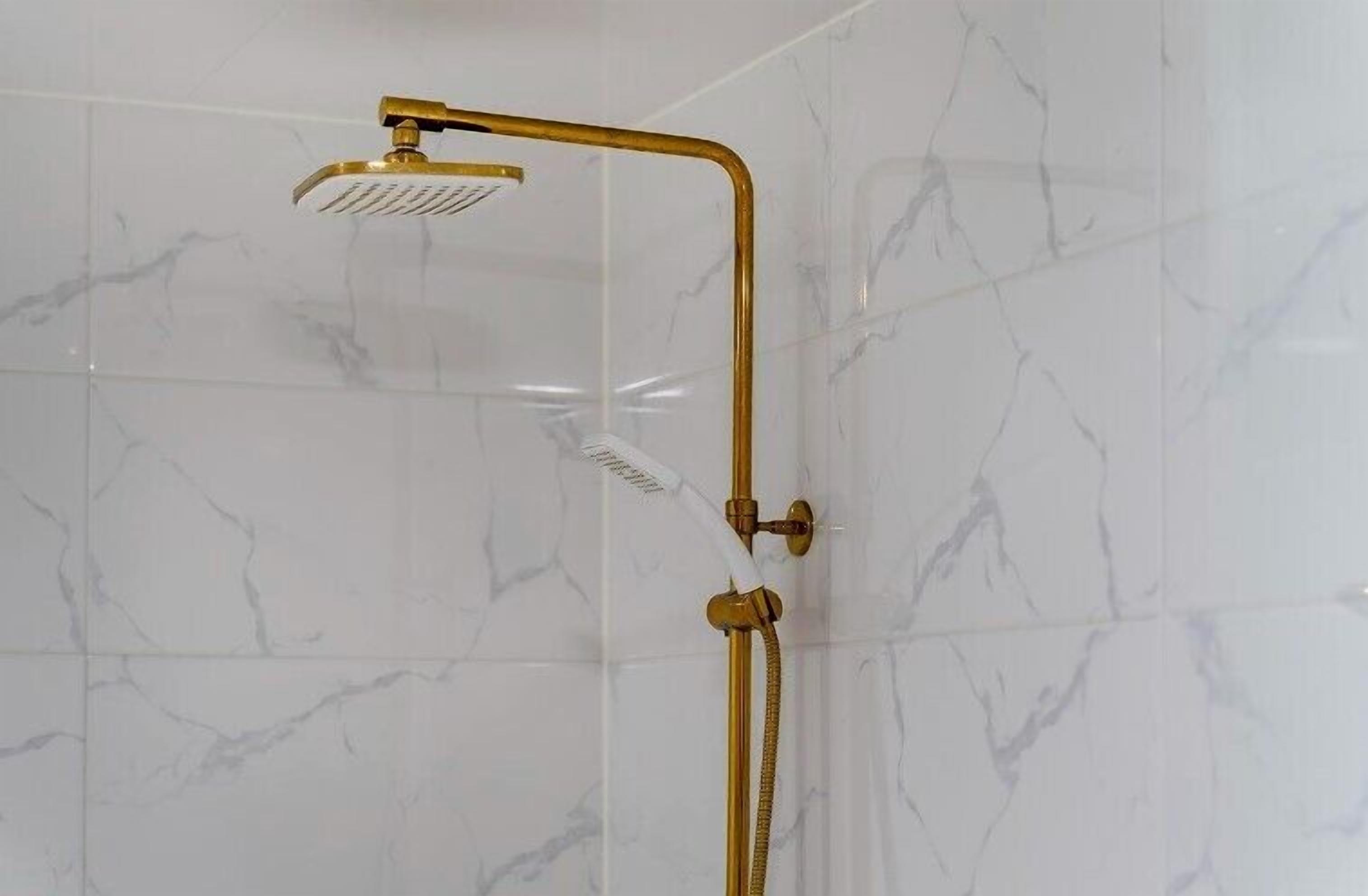 A shower with a gold showerhead and hose, set against a white marble wall.