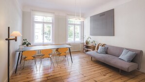 A modern living room with a sofa, a dining table with chairs, and a large window providing natural light. - Art & Design Parkview Apartment in Rīga (Rīga)