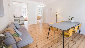 A modern living room with a grey sofa, wooden flooring, and a dining area with a grey table and yellow chairs. - Art & Design Parkview Apartment in Rīga (Rīga)