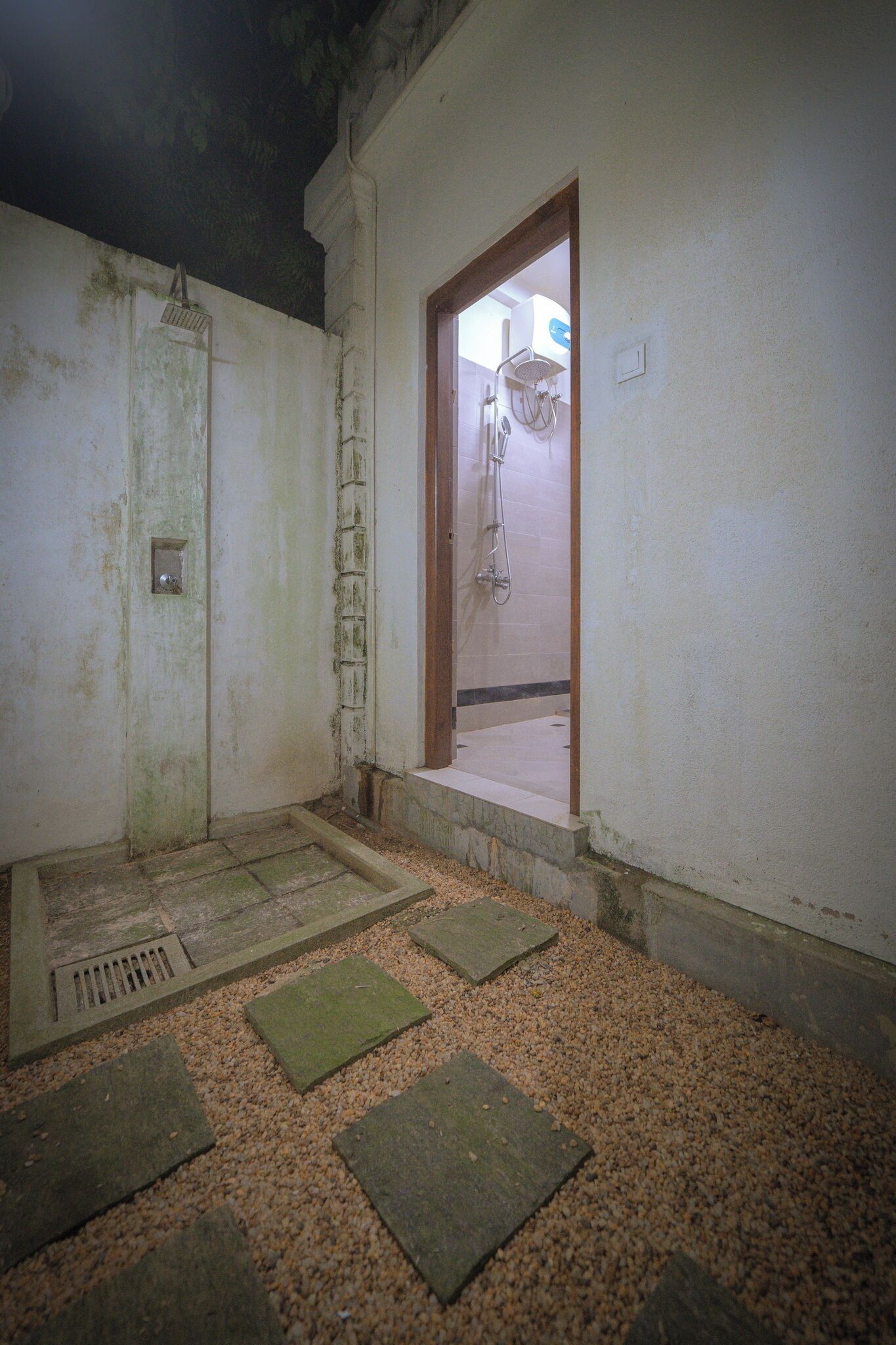 Una habitación pequeña y poco iluminada, con zona de ducha, una puerta que da a otra habitación y un ventanal con vistas.