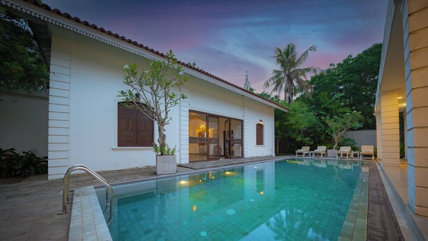 A swimming pool with a tiled deck, a covered outdoor area with seating, and a building with a tiled roof and windows. - Idda Bouqtiue Villa  (Ahangama)