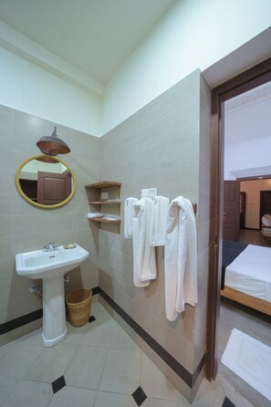 Un baño con lavamanos, espejo, toallero y una puerta que da a un dormitorio.