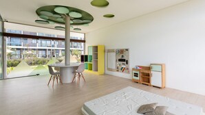 Una habitació infantil moderna amb un finestral gran, una taula rodona i un llit.