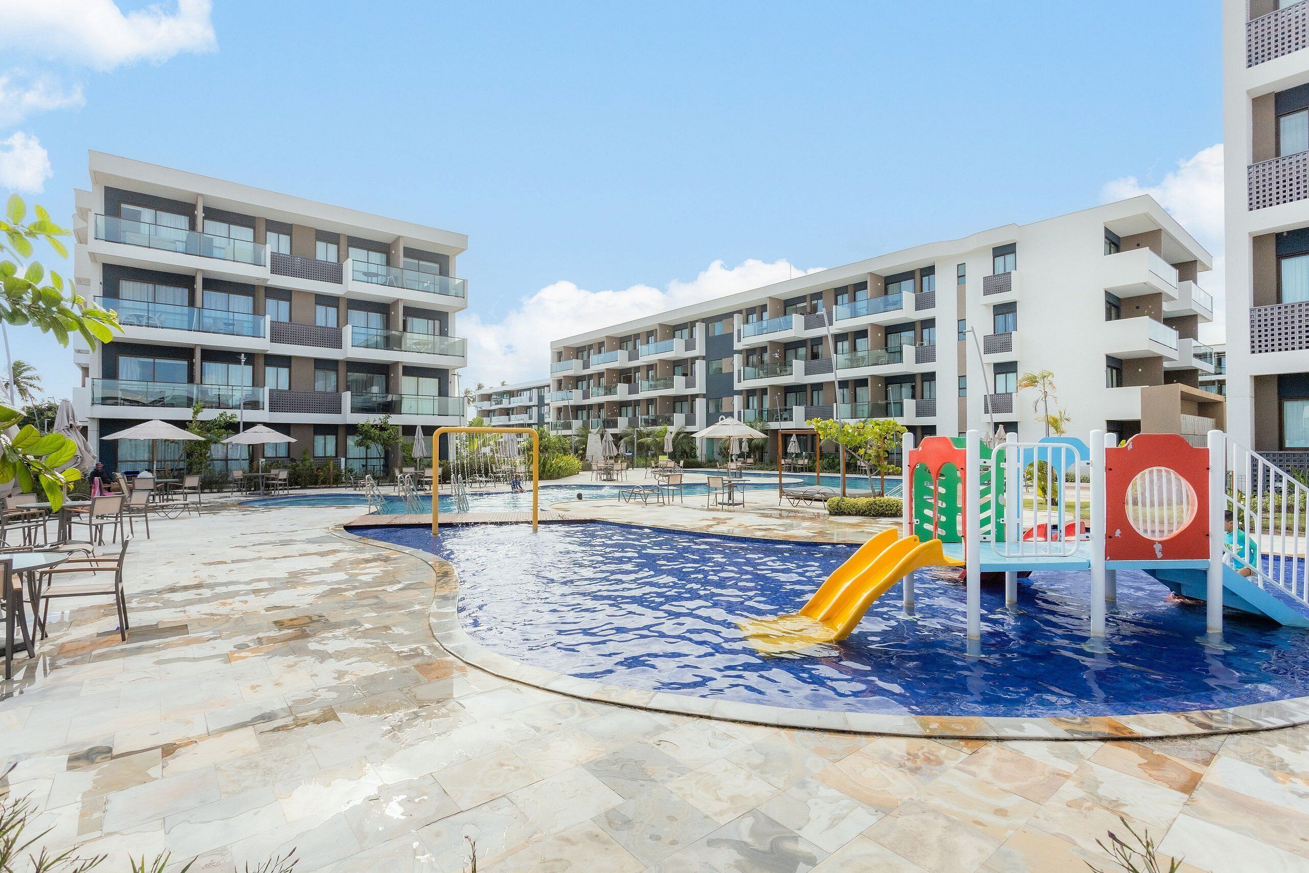 Zona de piscina con tobogán, rodeada de edificios modernos con balcones.