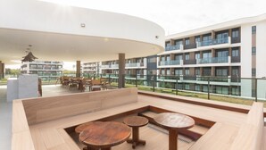 Zona d'estar exterior moderna amb taules i bancs de fusta, amb vista a un edifici residencial amb balcons.