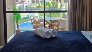 Habitació d'hotel amb llit, finestra que dona a una piscina i seients a l'aire lliure, i una planta en test.