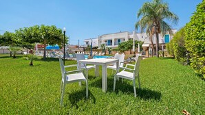 Un espace aménagé au bord de la piscine, avec une table et des chaises, une piscine, et un bâtiment en arrière-plan.
