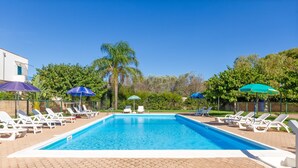 Une piscine rectangulaire avec une terrasse carrelée, entourée de chaises longues blanches et de parasols.