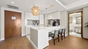 A modern kitchen with a central island, white cabinetry, and a wooden door. - Snug Studio in Dubai Mall Steps From Burj Khalifa (Dubai)