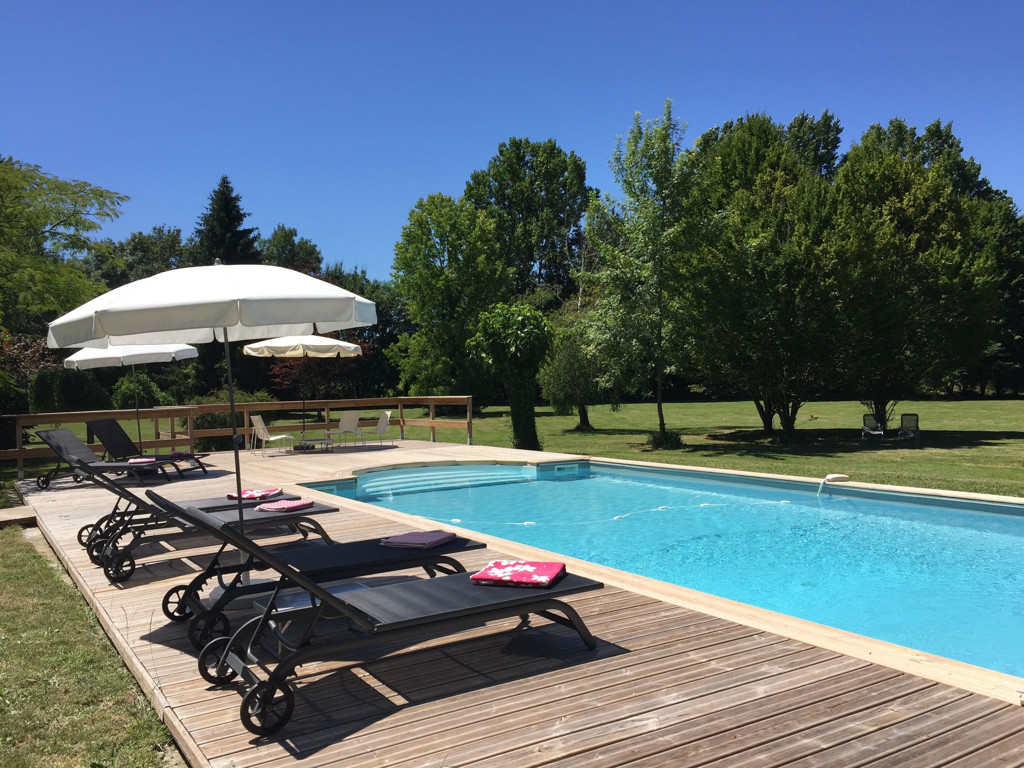 Una piscina con cubierta de madera, sillas de descanso y sombrillas.