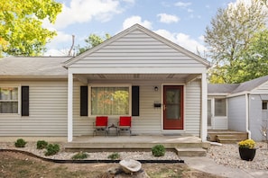 A single-story house with a front porch, two chairs, a small table, and a mailbox.