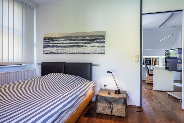 Una camera d'albergo moderna con un letto, un quadro raffigurante l'oceano, una scrivania con una lampada e una televisione.