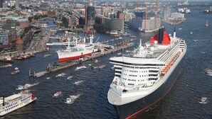 A large cruise ship docked at a port with a cityscape in the background.