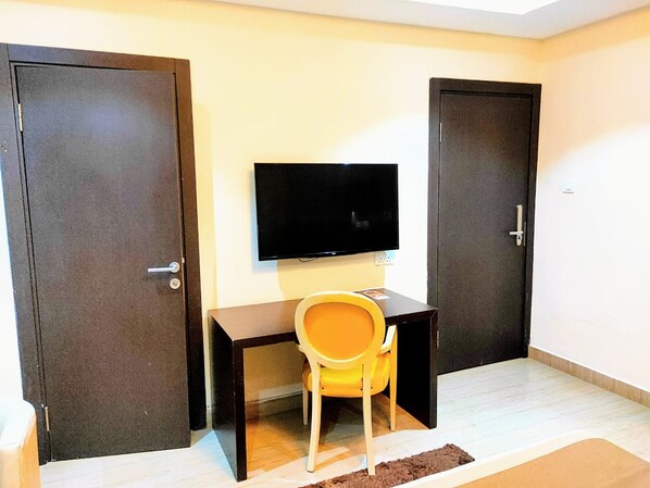A room with a desk, a chair, a television, and two doors. - The Cabin Hotel (Accra)