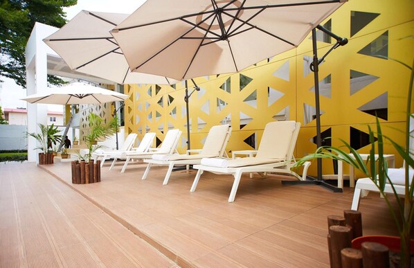 A poolside area with lounge chairs, umbrellas, and a yellow patterned wall. - The Cabin Hotel (Accra)