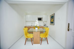 Een moderne keuken met witte kasten, een eettafel met glazen blad en gele stoelen.
