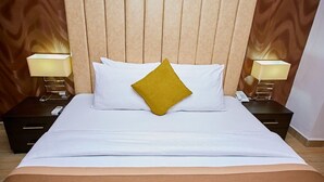 A hotel room with a wooden headboard, white bedding, a single mustard-colored pillow, and bedside lamps. - The Cabin Hotel (Accra)