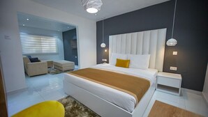 A modern bedroom with a large bed, bedside tables, a sofa, and a yellow chair. - The Cabin Hotel (Accra)