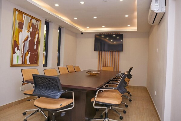 A conference room with a long table, chairs, a flat-screen TV, and a painting on the wall. - The Cabin Hotel (Accra)