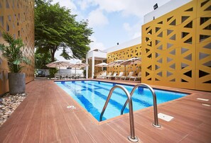 A swimming pool with a wooden deck, lounge chairs, and umbrellas. - The Cabin Hotel (Accra)