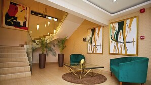 A modern interior with a staircase, a glass table, teal armchairs, and abstract paintings. - The Cabin Hotel (Accra)