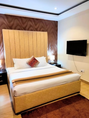 A hotel room with a large bed, a flat-screen TV mounted on the wall, and a nightstand with a lamp. - The Cabin Hotel (Accra)