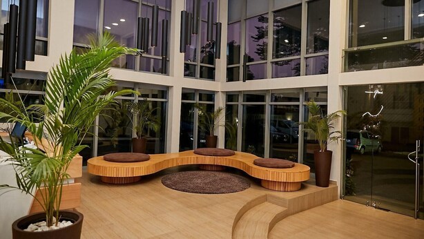 A spacious lobby with large windows, a curved seating area, and potted plants. - The Cabin Hotel (Accra)