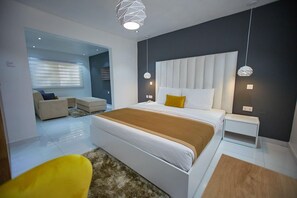 A modern bedroom with a large bed, bedside tables, a sofa, and a yellow chair. - The Cabin Hotel (Accra)