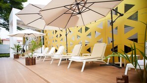 A poolside area with lounge chairs, umbrellas, and a yellow patterned wall. - The Cabin Hotel (Accra)