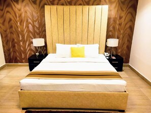 A hotel room with a large bed, two bedside tables, a wooden headboard, and a patterned wall. - The Cabin Hotel (Accra)