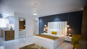 Ein modernes Schlafzimmer mit einem großen Bett, Nachttischen, einem Spiegel und einer kleinen Küchenzeile.