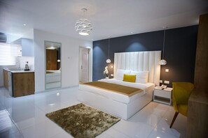 A modern bedroom with a large bed, bedside tables, a mirror, and a small kitchen area. - The Cabin Hotel (Accra)