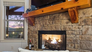 A stone fireplace with a log fire, a bottle of wine, and a glass on a table. - Mountain-View Adventures • Gym, Hot Tub, Fire Pit (Blue Ridge)