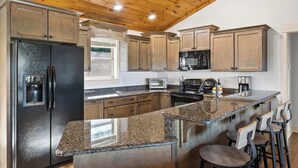 A kitchen with granite countertops, wooden cabinets, stainless steel appliances, and a bar area with stools. - Mountain-View Adventures • Gym, Hot Tub, Fire Pit (Blue Ridge)