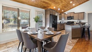 A modern kitchen with wooden cabinets, a central island, and a dining area with a table set for four. - Mountain-View Adventures • Gym, Hot Tub, Fire Pit (Blue Ridge)