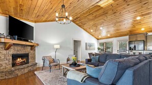 A spacious living room with a stone fireplace, a large gray sectional sofa, and a wooden ceiling. - Mountain-View Adventures • Gym, Hot Tub, Fire Pit (Blue Ridge)